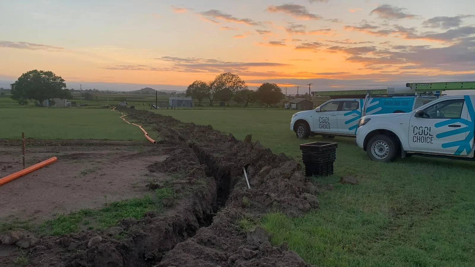 Sunset over a Lockyer Valley paddock with a freshly dug cable trench and two white Cool Choice utes