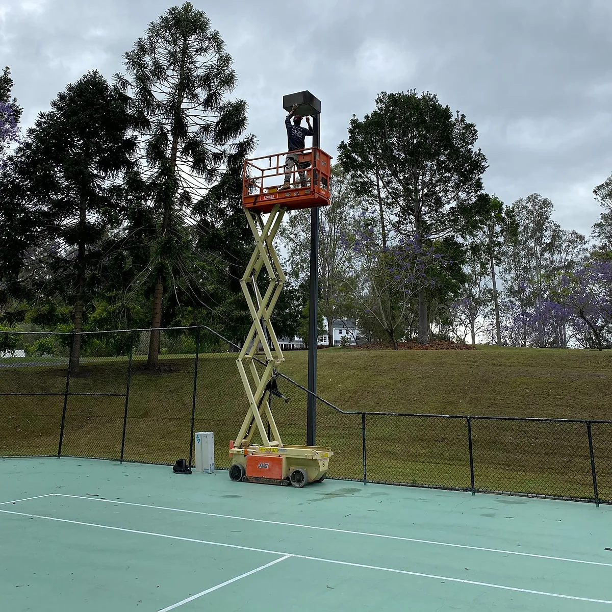 A Cool Choice electrician on a scissor lift working on a tennis court light pole