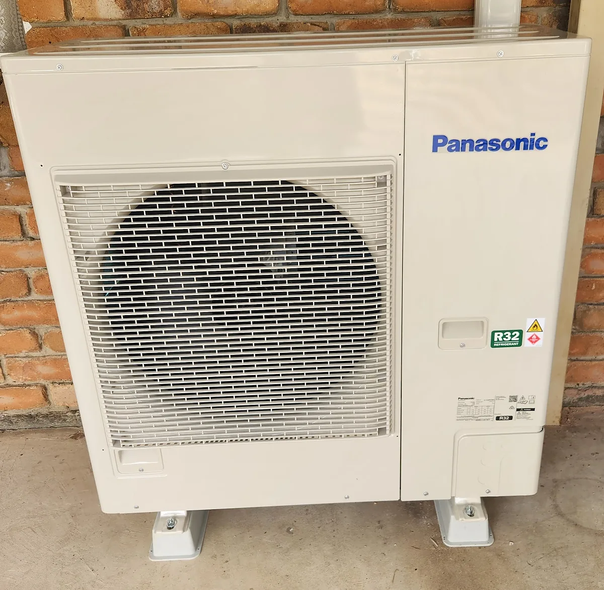 A large Panasonic ducted outdoor unit on feet against a brick wall