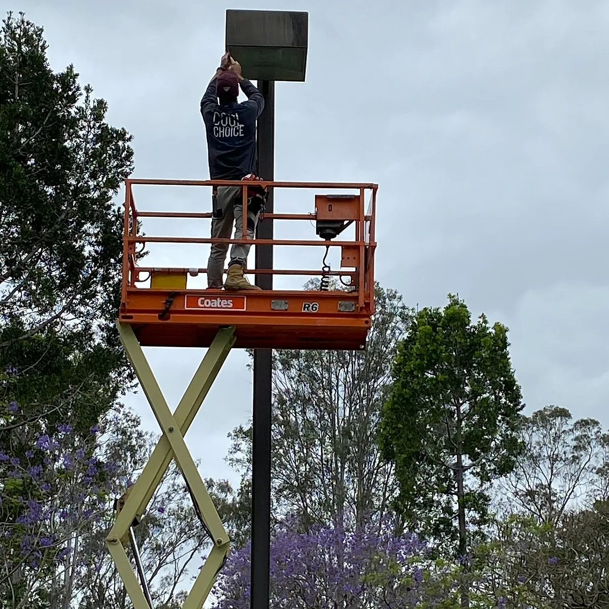 A Cool Choice electrician on an orange scissor lift fixing a light at the top of a pole