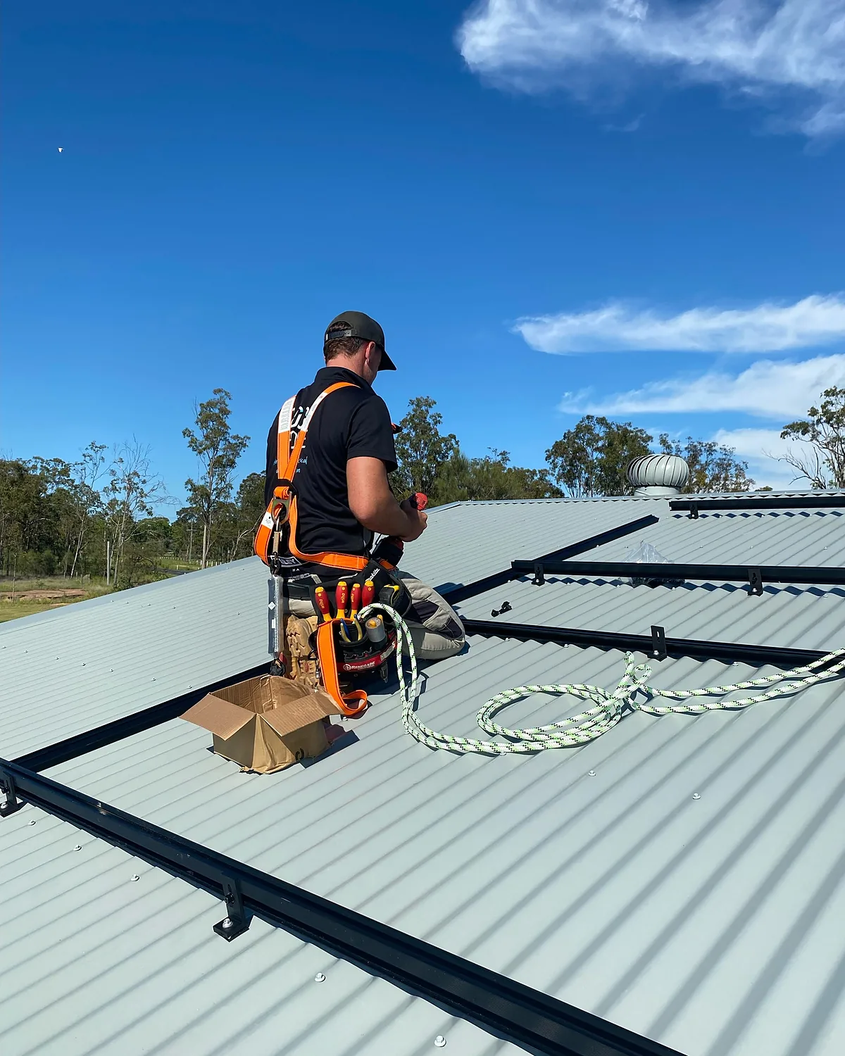 An installer in a safety harness fitting solar rails on a metal roof