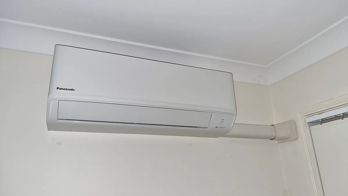 A Panasonic split system installed above a window in a bedroom with a neat pipe cover