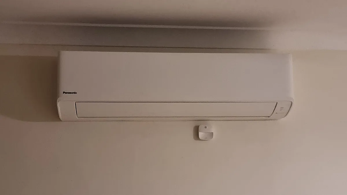 A Panasonic split system head on a living room wall with a wall controller below