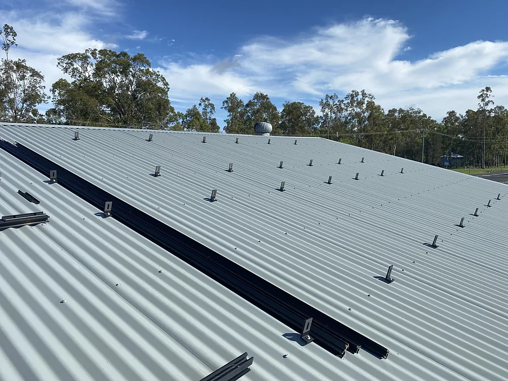 Solar mounting rails fixed across a grey metal roof under a blue sky