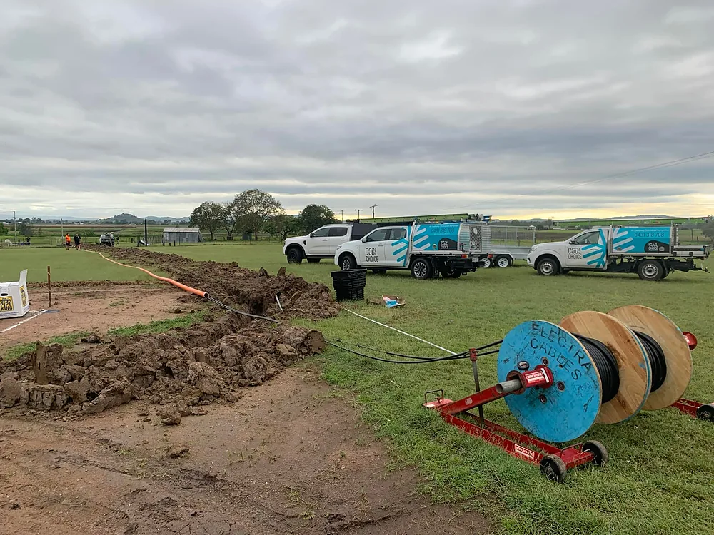 A long cable trench across a paddock with a cable drum and three Cool Choice utes